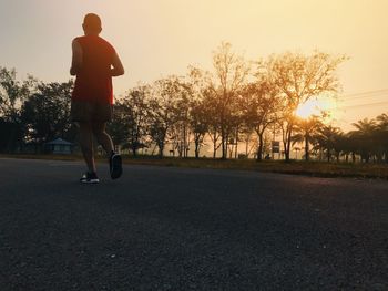 Rear view of man skateboarding on street against sky during sunset