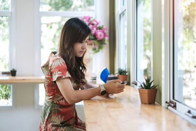 Side view of woman using smart phone sitting by window at cafe