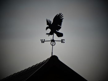 Low angle view of weather vane on roof against sky