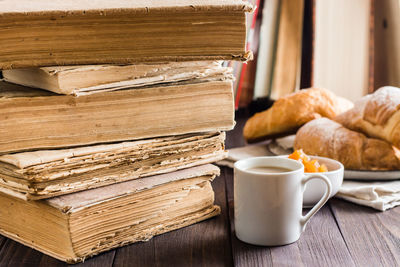 A cup of coffee and a plate with croissants in a vintage library with books on a wooden table. 