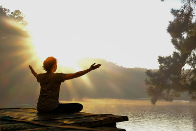 Rear view of woman with arms raised against sky during sunset