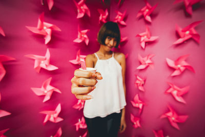 Portrait of young woman holding pink standing against gray background