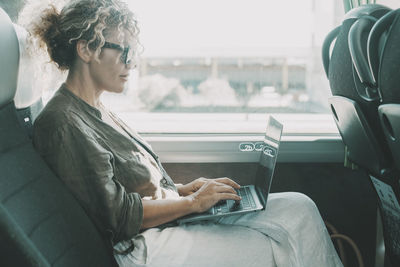 Side view of woman using mobile phone while sitting in bus