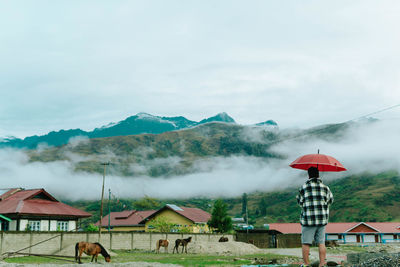 Rear view of woman holding umbrella against sky
