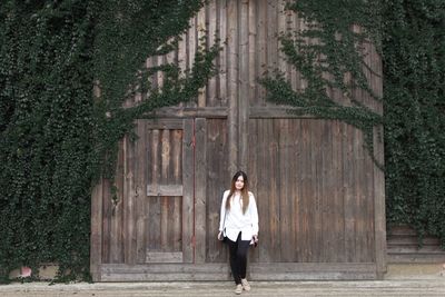 Full length portrait of young woman standing by wooden door