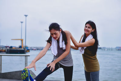 Portrait of smiling woman assisting friend in exercising at beach