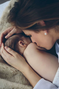 Mother kissing shirtless daughter while lying down on bed at home