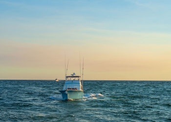 Fishing boat on sea against sky during sunset