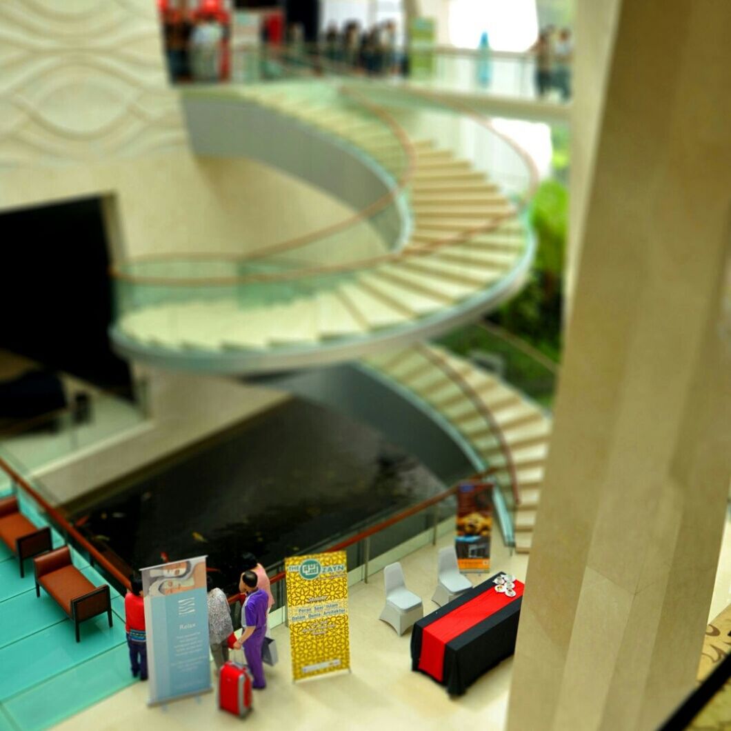 indoors, high angle view, table, focus on foreground, text, incidental people, architecture, railing, built structure, day, men, communication, book, close-up, person, chair, selective focus