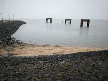 Wooden posts in sea against clear sky