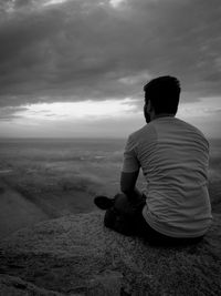 Rear view of man sitting on land against sky