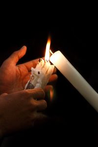 Close-up of hand holding burning candle against black background