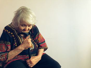 Thoughtful senior woman with walking cane sitting against wall