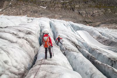 Rear view of hikers on glacier against rocky mountains