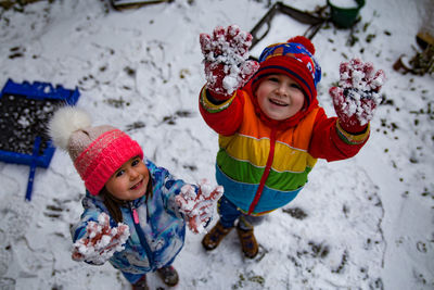 High angle portrait of cute siblings standing on snow covered field