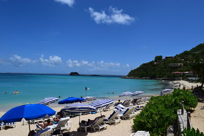 Parasols and lounge chairs at beach against blue sky