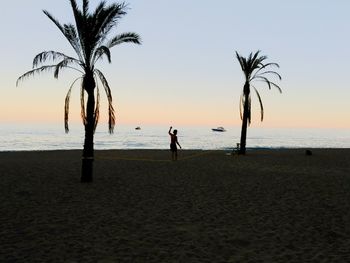 Man balancing on tightrope at beach against sky during sunset