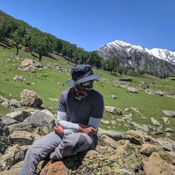 Rear view of man sitting on rock against mountains