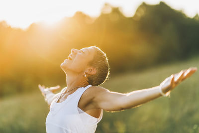 Side view of woman with arms raised standing outdoors