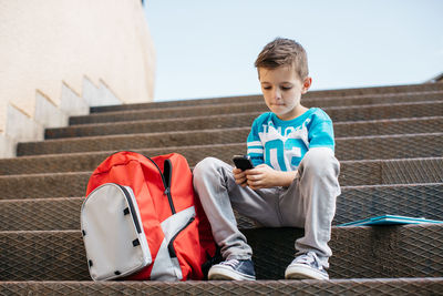 Full length of boy using on mobile phone while sitting on steps