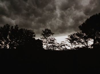 Low angle view of silhouette trees against storm clouds