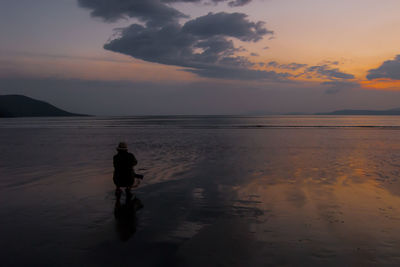 Silhouette man on beach against sky at sunset