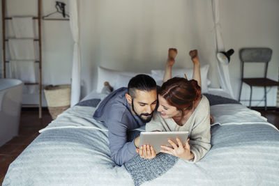 Couple using digital tablet while lying on bed at home