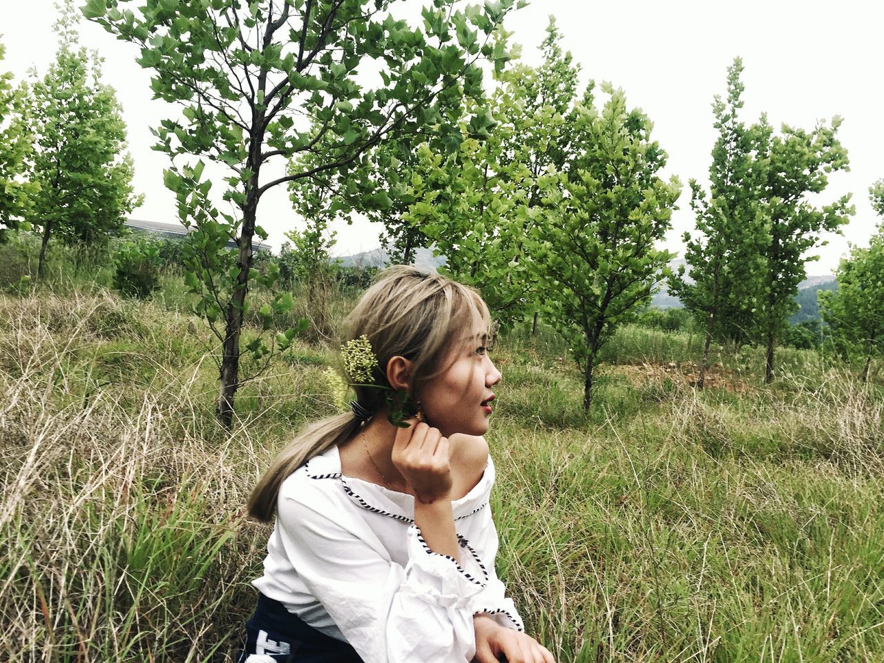 WOMAN STANDING ON FIELD AGAINST TREES