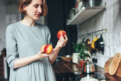 Young woman holding apples while standing in kitchen at home