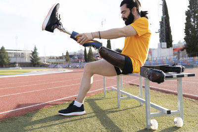 Bearded man removing prosthetic leg sitting on bench