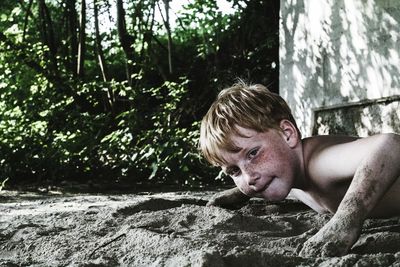 Shirtless boy playing in sand against plants