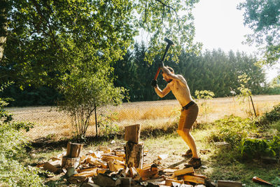 Full length of shirtless man standing by tree in forest