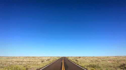 Road amidst field against clear blue sky