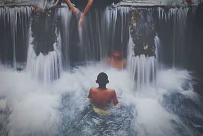 Shirtless men enjoying at waterfall