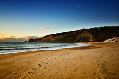 Scenic view of beach against clear sky at sunset