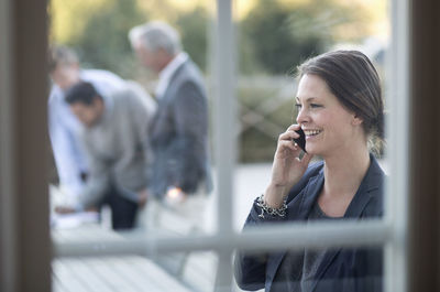 Businesswoman using mobile phone at patio with colleagues working in background