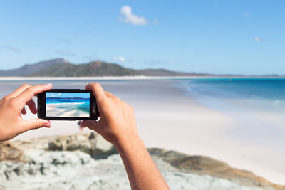 Midsection of person photographing sea against sky