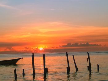 Silhouette wooden posts in sea against sky during sunset