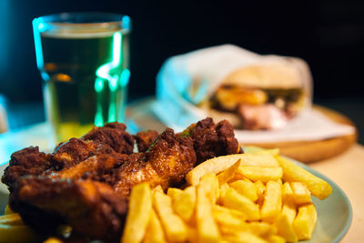 Close-up of food on table with sandwich in backgroud with beer and chicken wings and fried chips