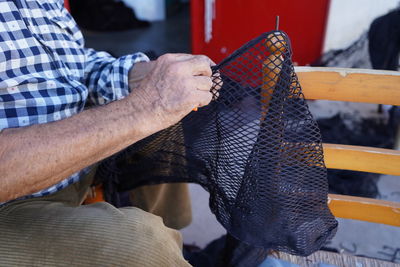 Midsection of man working on fishing net