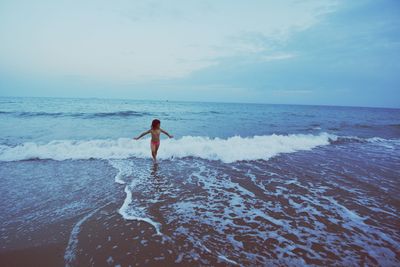Shirtless girl wading in sea against sky