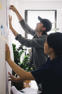 Male and female architect colleagues discussing over blueprint on wall at home office