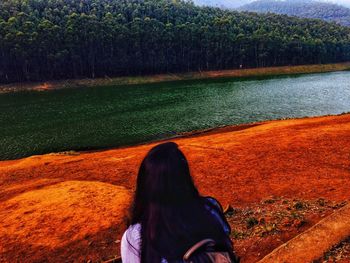 Rear view of woman looking at lake against trees