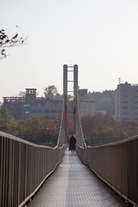 Man standing on footbridge in city against clear sky