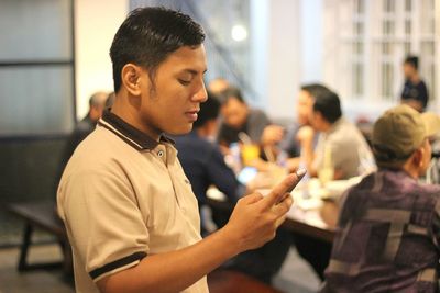 Side view of young man using smart phone while standing in restaurant