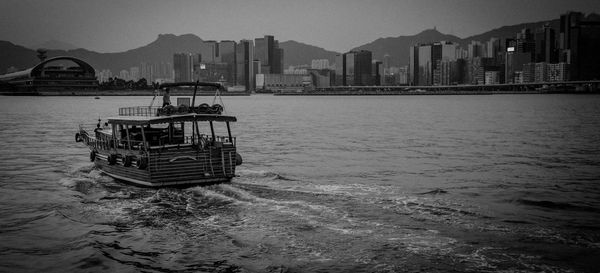 Ferry sailing in sea by city against sky