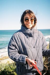 Portrait of smiling woman standing by sea against sky