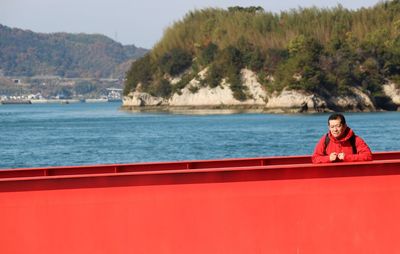 Portrait of man on red bridge at port against trees