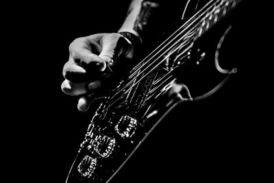 Close-up of hand playing guitar against black background