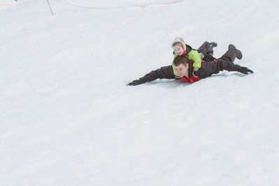 Man with daughter sliding on snow covered field